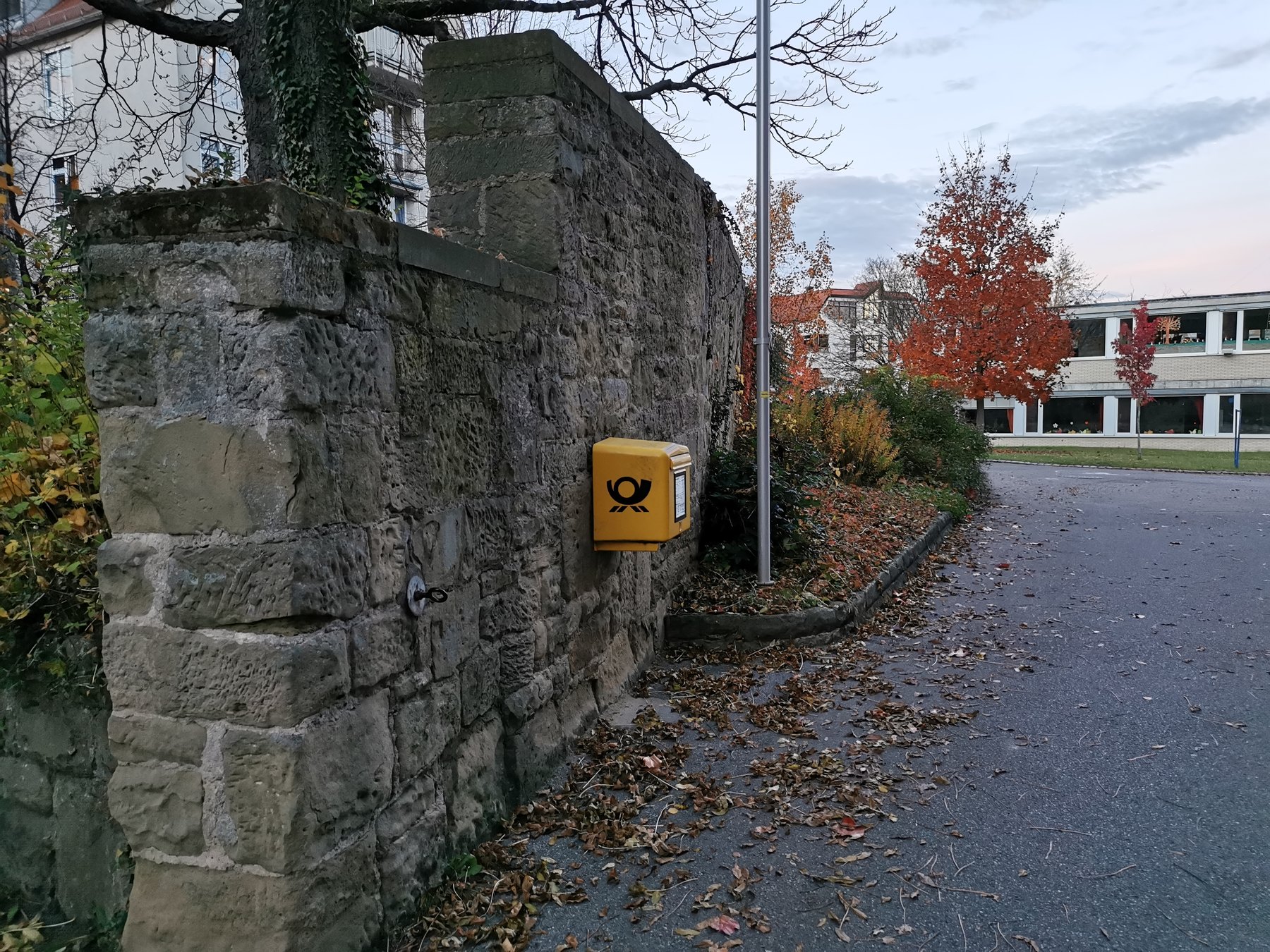 Alte Schlossmauer mit gelbem Deutsche-Post-Briefkasten an einer herbstlichen Straße